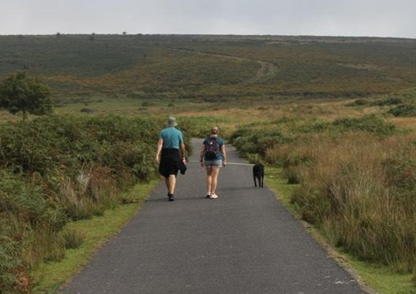 Two people walking a dog on a path through a grassy landscape in Devon