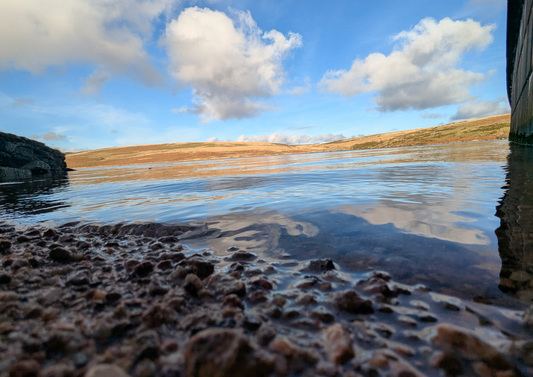 Rocks at the edge of a reservoir with a view of the sky and clouds.